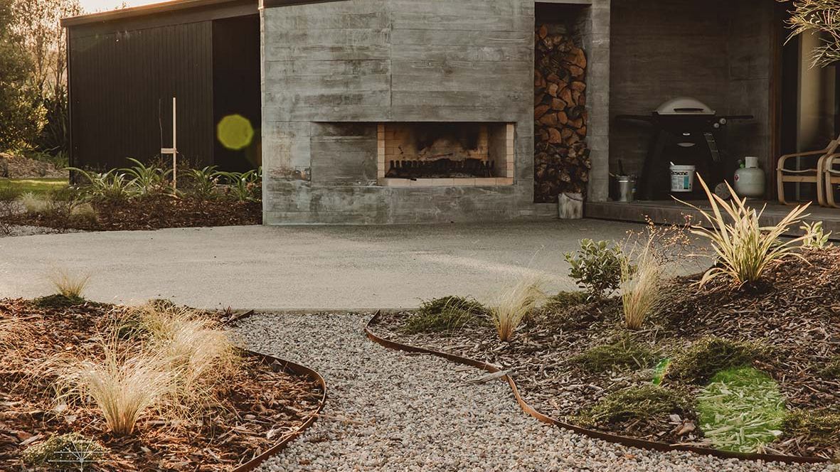 Curved pebble garden path with metal edging and ornamental grasses leading to an outdoor fireplace